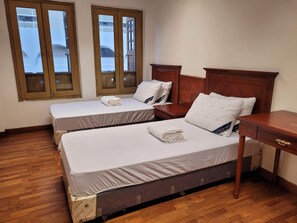 Habitación de hotel con dos camas individuales, cabeceros de madera, una pequeña mesa de madera y una ventana con vistas a edificios.