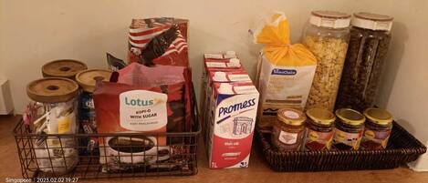 A variety of food items including a carton of milk, a bag of bread, and jars of preserves on a table.