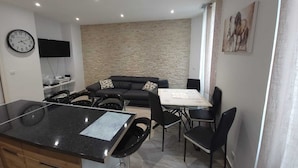 A modern living room with a stone wall, a black sofa, and a dining table with chairs. - Luxurious apartment, wifi, air conditioning, 50M from the beach (Nice)