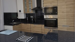 A modern kitchen with black countertops, wooden cabinets, a built-in oven, and a black range hood. - Luxurious apartment, wifi, air conditioning, 50M from the beach (Nice)