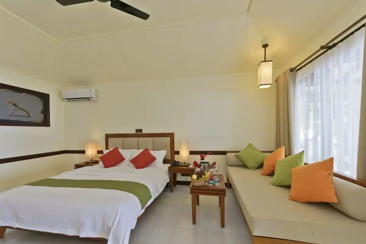 A hotel room with a bed, a sofa, a nightstand, a lamp, and a ceiling fan.