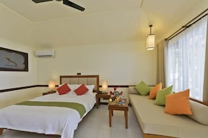 Quarto de hotel com cama, sofá, mesa de cabeceira, luminária e ventilador de teto.