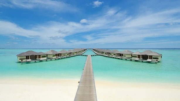 A long wooden pier leading to overwater bungalows with a clear blue sky above.