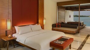 A modern hotel room with a large bed, a seating area with a view of the sea, and a wooden accent wall.