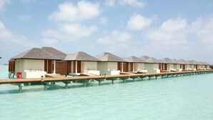 Overwater bungalows with a row of rooms connected by a wooden deck over clear turquoise water.