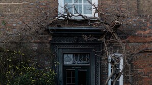 A brick building with a black door labeled "BALLARDS," a white window, and a green metal fence. - Design-Led- 2xSuper-King Beds- Ensuites- W Parking  (Eton)