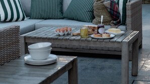 A cozy outdoor seating area with a wicker sofa, a wooden table with a spread of food and drinks, and a wicker chair. - Design-Led- 2xSuper-King Beds- Ensuites- W Parking  (Eton)