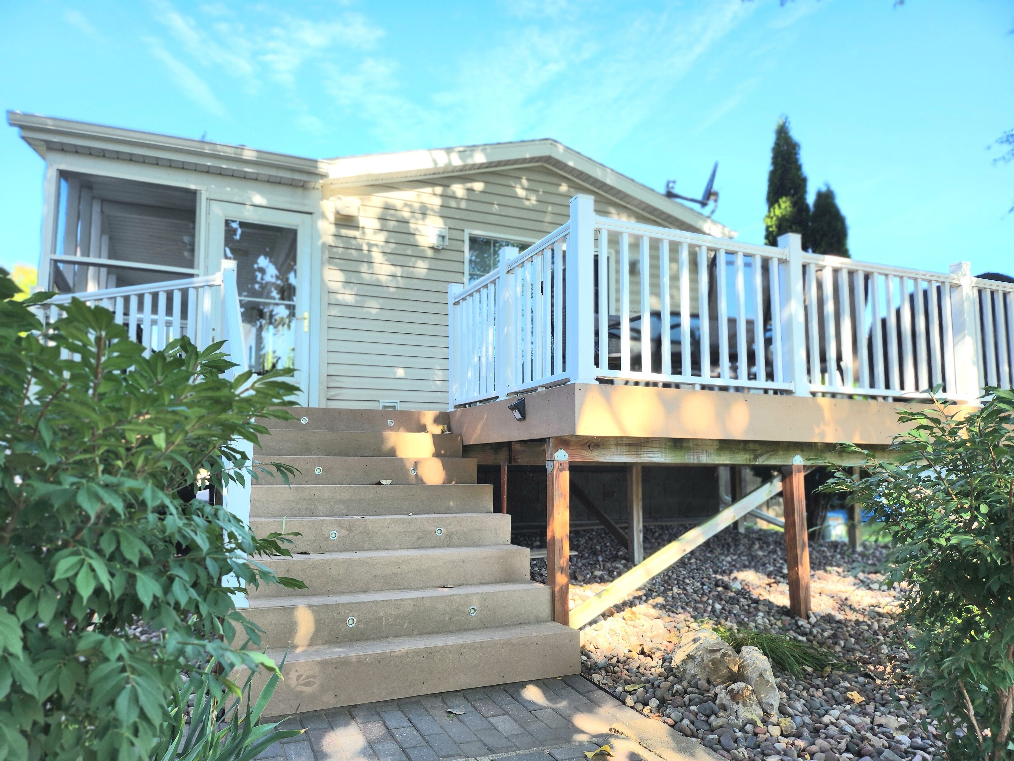 A two-story house with a wooden deck and a set of concrete stairs leading to the entrance.