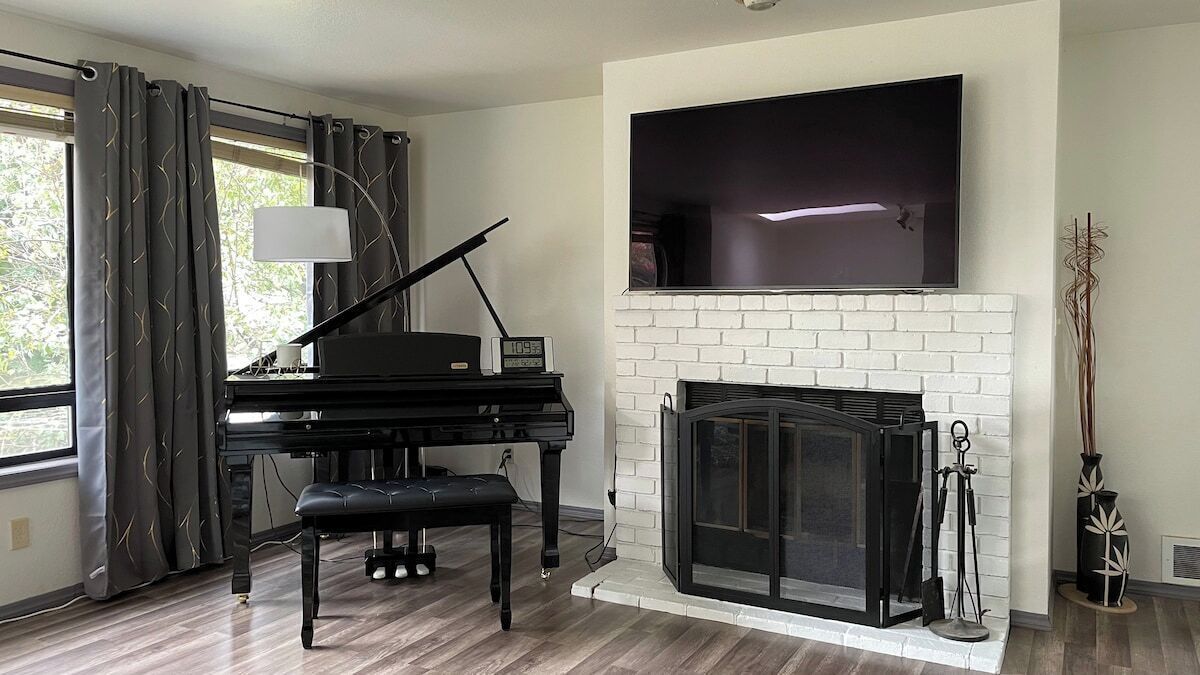 A living room with a piano, a fireplace, and a TV mounted above it.