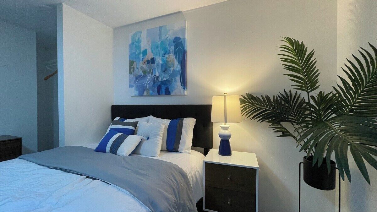 Une chambre à coucher avec un lit, une table de chevet, une lampe et une grande plante en pot.