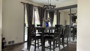 A dining area with a round table and four chairs, a vase with flowers, and a large mirror reflecting the room. - Remodel Spacious Modern Retreat (Shoreline)