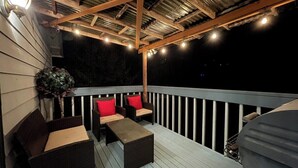An outdoor deck with a railing, wooden furniture, and string lights. - Remodel Spacious Modern Retreat (Shoreline)