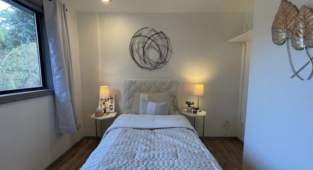 A bedroom with a bed, two bedside tables, a wall art piece, and a window with curtains.