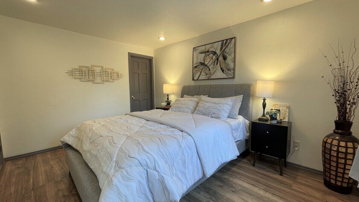 Un dormitorio con una cama, mesitas de noche, un reloj de pared y un jarrón decorativo.
