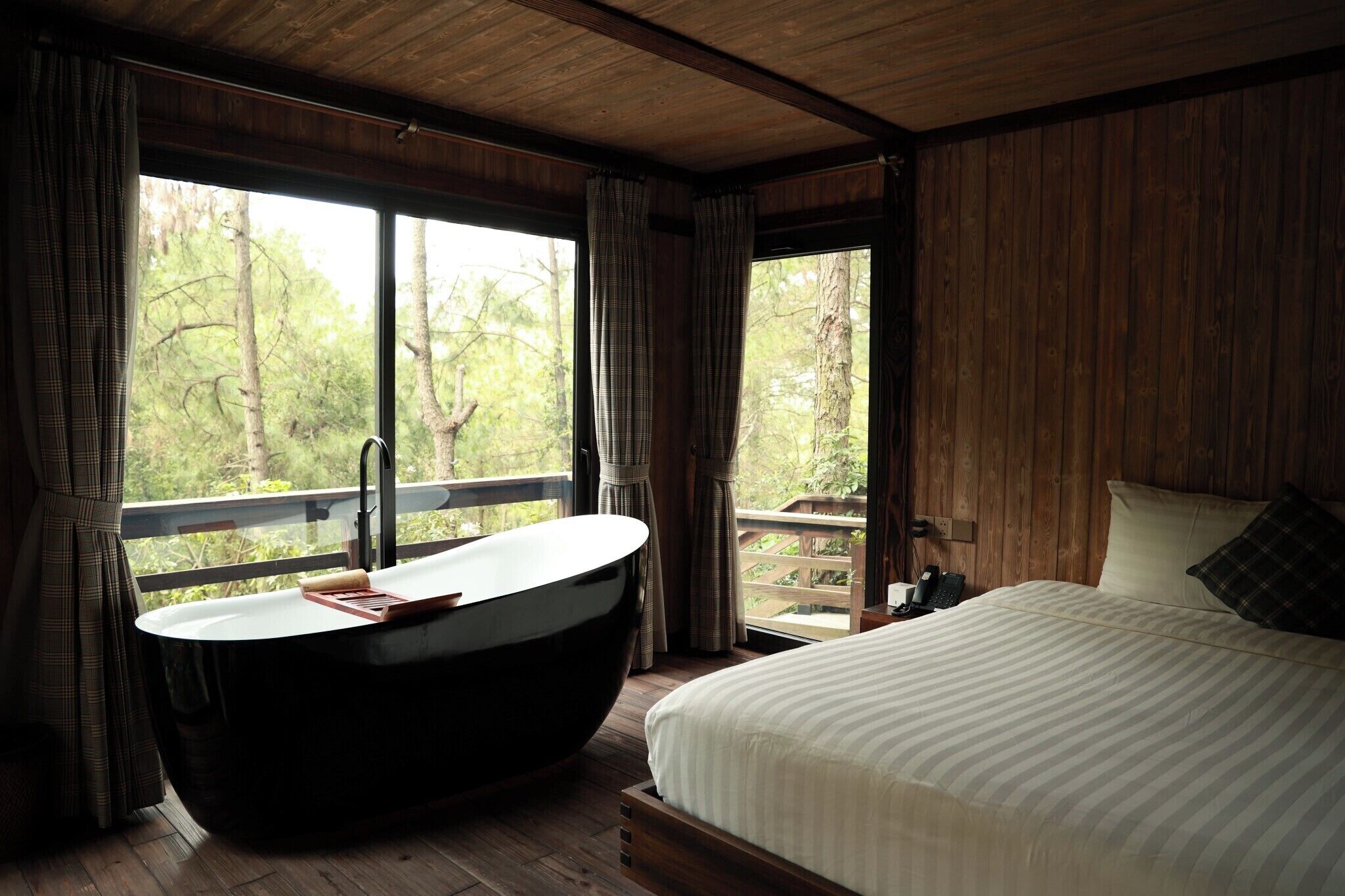 Un dormitorio con una cama grande, una bañera independiente y vistas al exterior a través de amplios ventanales.