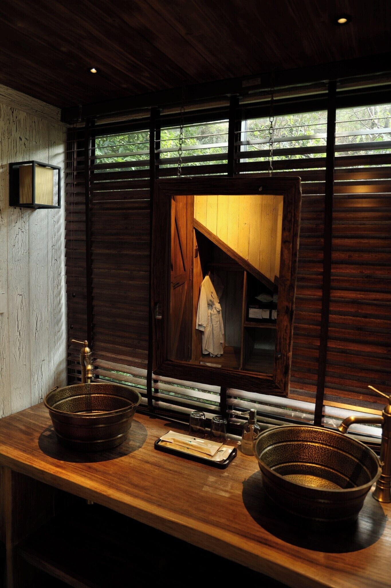A rustic bathroom with wooden walls, a large mirror, and a wooden vanity with two basins.