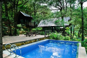 A pool area with a wooden deck, a picnic table, and a small building surrounded by trees. - Amaya Retreat (Hanoi)