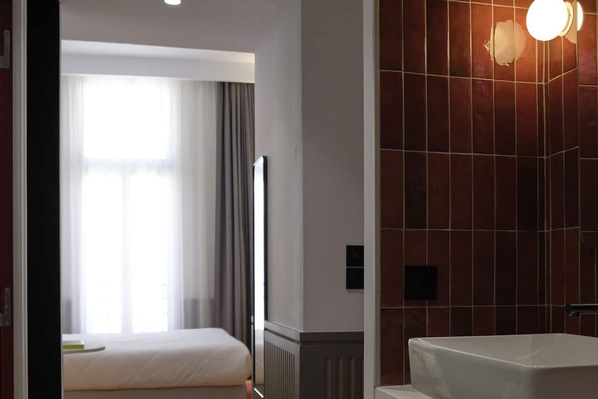 A hotel room with a bed, a bathroom with a sink, and a window with curtains.