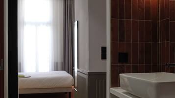 Quarto de hotel com cama, banheiro com pia e janela com cortinas.