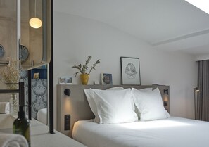 Moderni hotellihuone, jossa on suuri sänky, yöpöytä, peili ja ruukussa oleva kasvi.