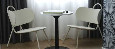 A room with a round table and two white chairs, a window with curtains, and a patterned wall.