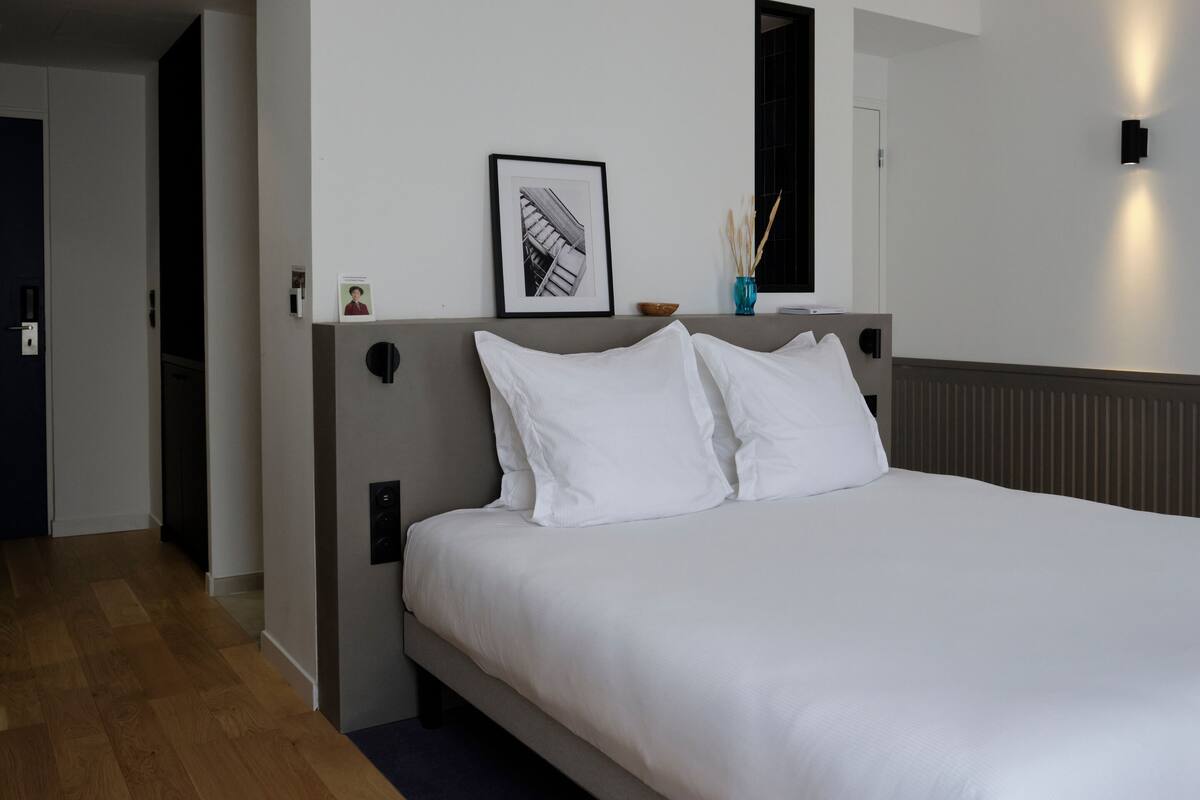 A neatly made bed with white linens in a modern hotel room.