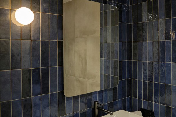 A bathroom with dark blue tiles, a white bathtub, and a towel hanging on the wall. - Maison Juste (Marseille)