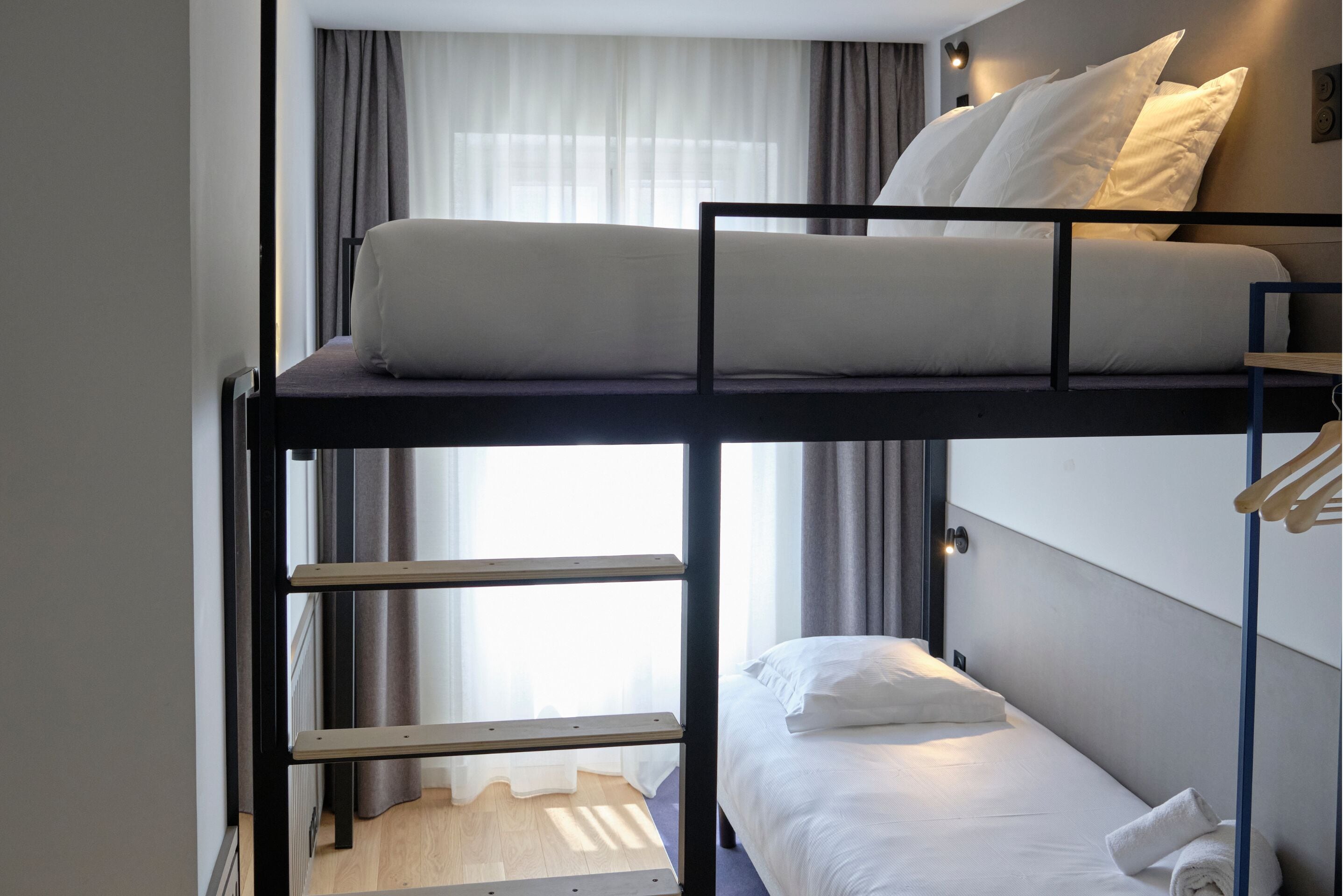 A bunk bed room with a window, curtains, and a small table.