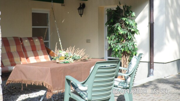 A dining area with a table set for two, a hanging plant, and a checkered sofa.