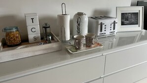 Una encimera de cocina con un tarro de frutos secos, un rollo de toallas de papel, un tostador y dos tazas.