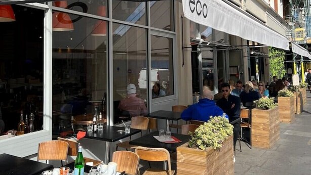 Un café al aire libre con mesas y sillas, un amplio ventanal y un letrero que dice "eco".