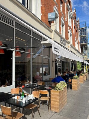 Un café al aire libre con mesas y sillas, un amplio ventanal y un letrero que dice "eco".