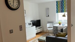 Una sala moderna con televisor de pantalla plana, un comedor con mesa y sillas, y un sofá.