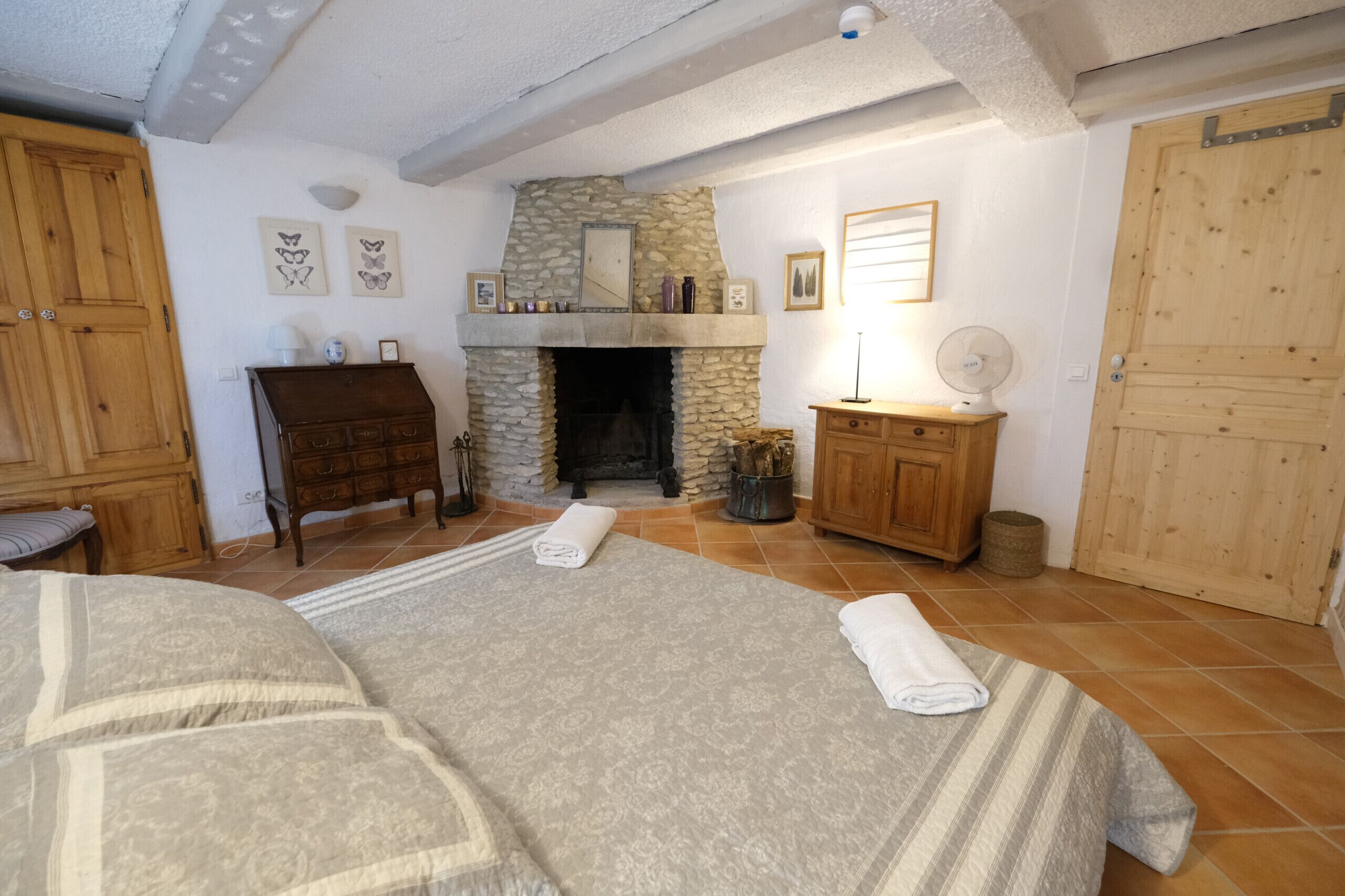 A cozy room with a stone fireplace, wooden furniture, and a bed with neatly folded towels.