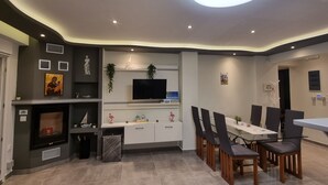 Ein modernes Wohnzimmer mit Kamin, Fernseher, Esstisch und Stühlen.