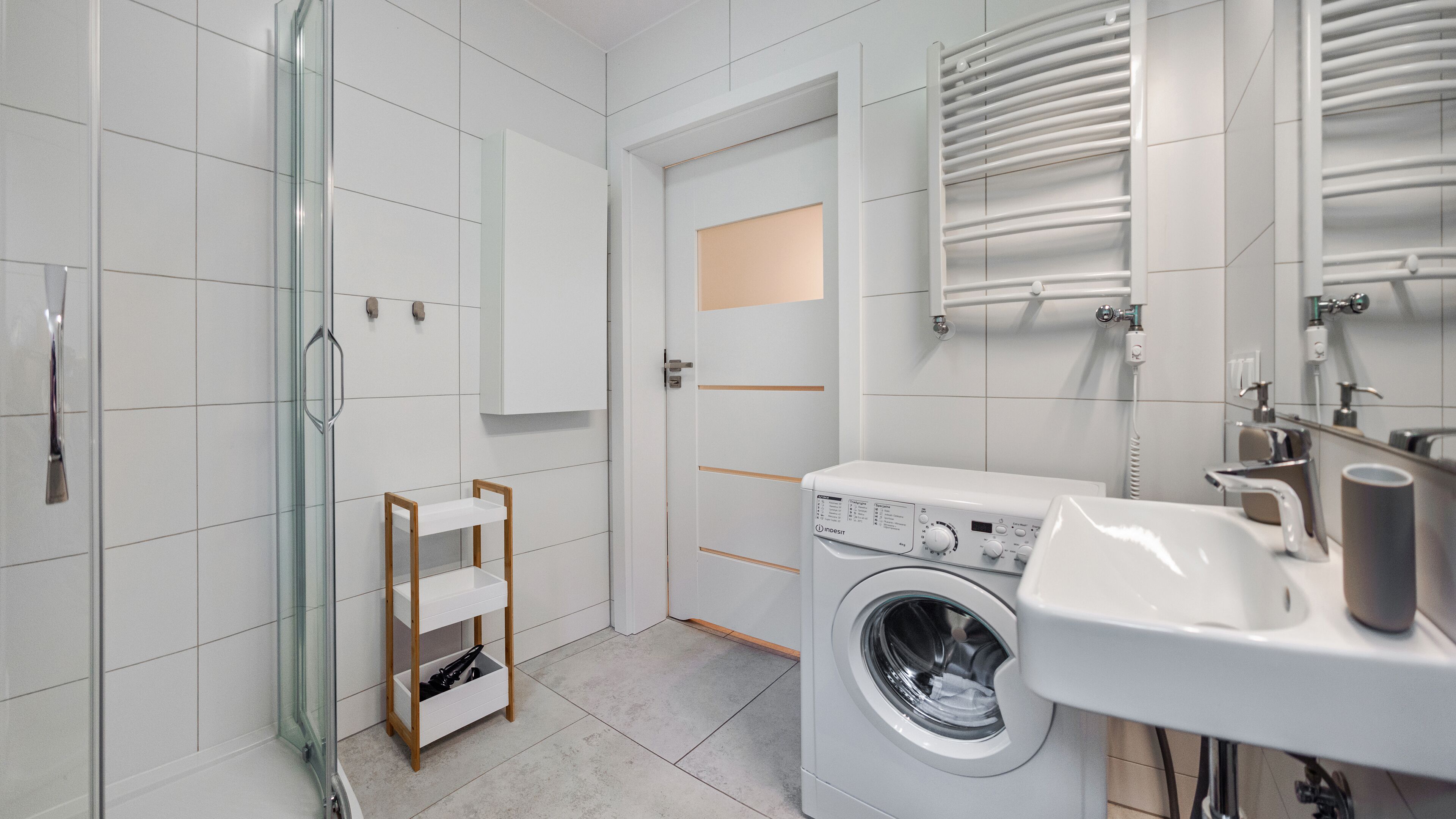 Ein modernes Badezimmer mit Duschkabine aus Glas, integrierter Waschmaschine und Waschbecken mit Spiegel.