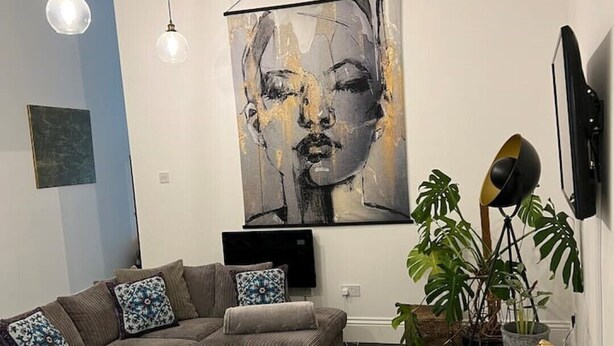 Un salon moderne avec un canapé d’angle, une table basse, un tapis à motifs et un grand tableau abstrait accroché au mur.
