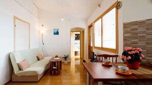 Una sala de estar acogedora con sofá, una mesa de comedor con sillas, televisor y planta en maceta.