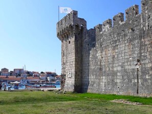 A historic stone castle with a flag, surrounded by a grassy area and a marina with boats. - Apartments Frano (Trogir)