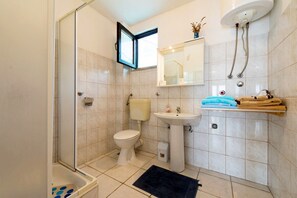 A bathroom with a glass shower enclosure, a toilet, a sink, and a towel rack with towels. - Apartments Frano (Trogir)