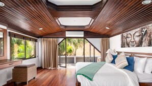 Ein geräumiges Schlafzimmer mit einem großen Bett, Holzboden, Deckenventilator und Blick ins Grüne.