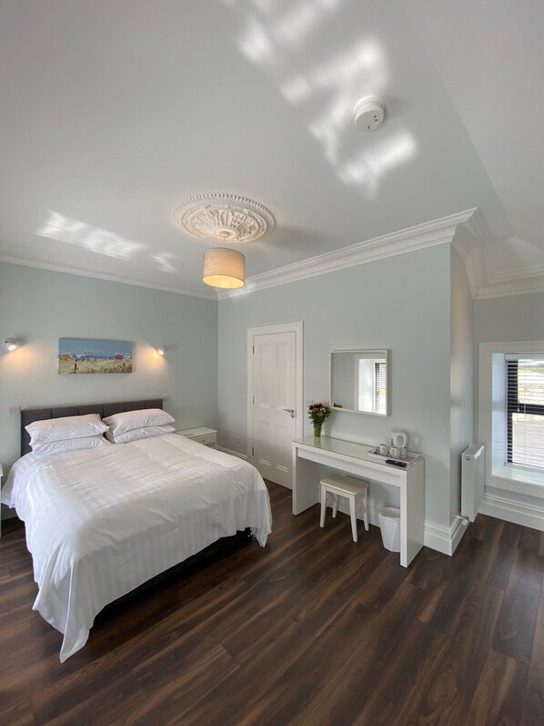 Une chambre à coucher avec un grand lit, une coiffeuse avec un miroir, un bureau et une fenêtre avec des stores.