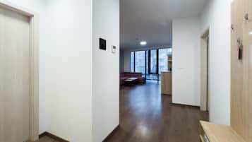 A hallway with wooden flooring, white walls, and a seating area with a sofa and table in the distance.