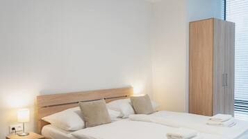 A modern hotel room with a wooden headboard bed, a nightstand with a lamp, and a wardrobe.