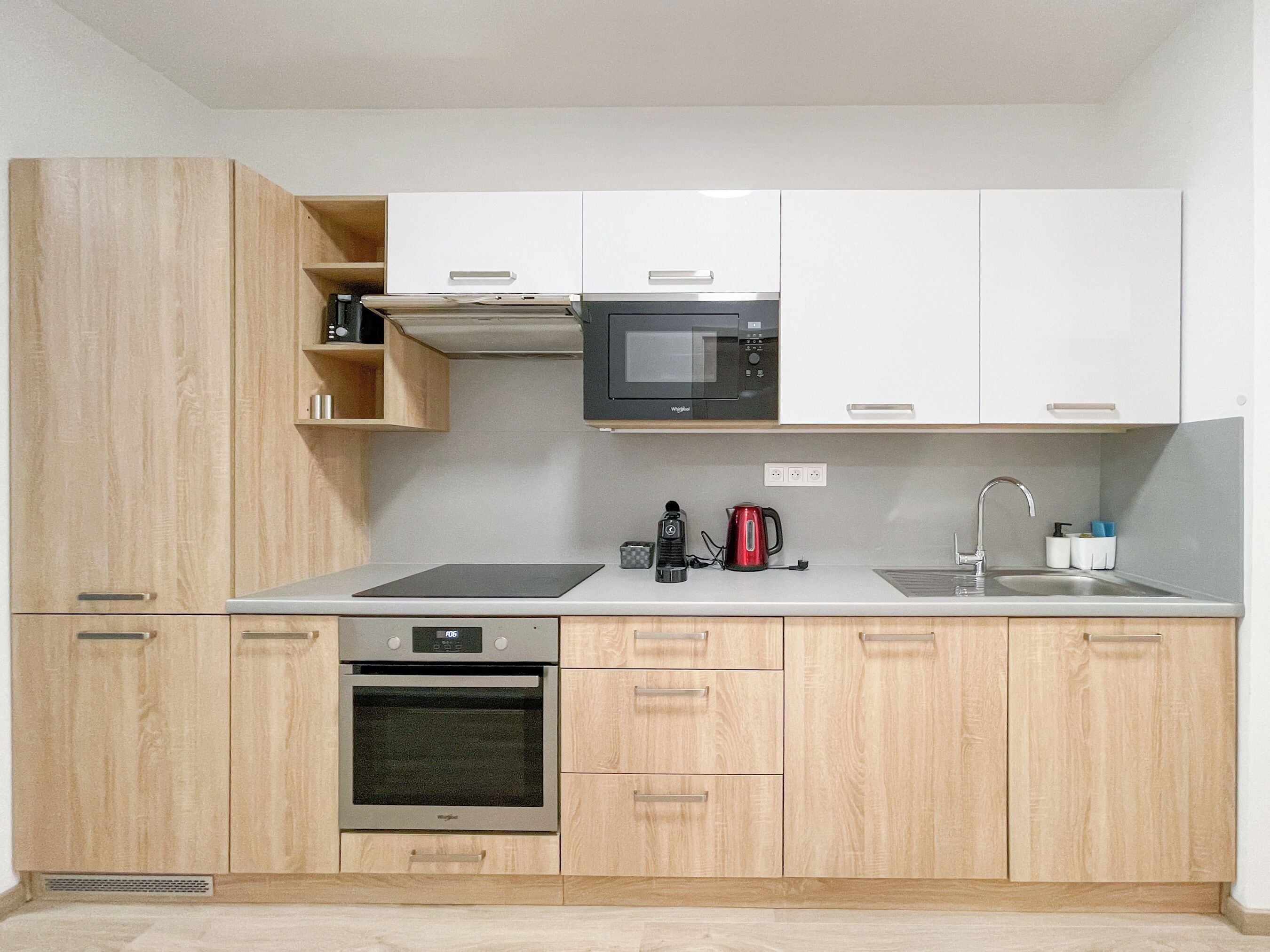 A compact kitchen with a microwave, kettle, coffee maker, and dishwasher.