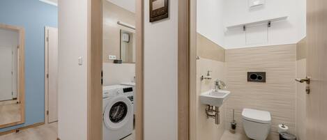 A modern bathroom with a washing machine, sink, toilet, and a mirror.