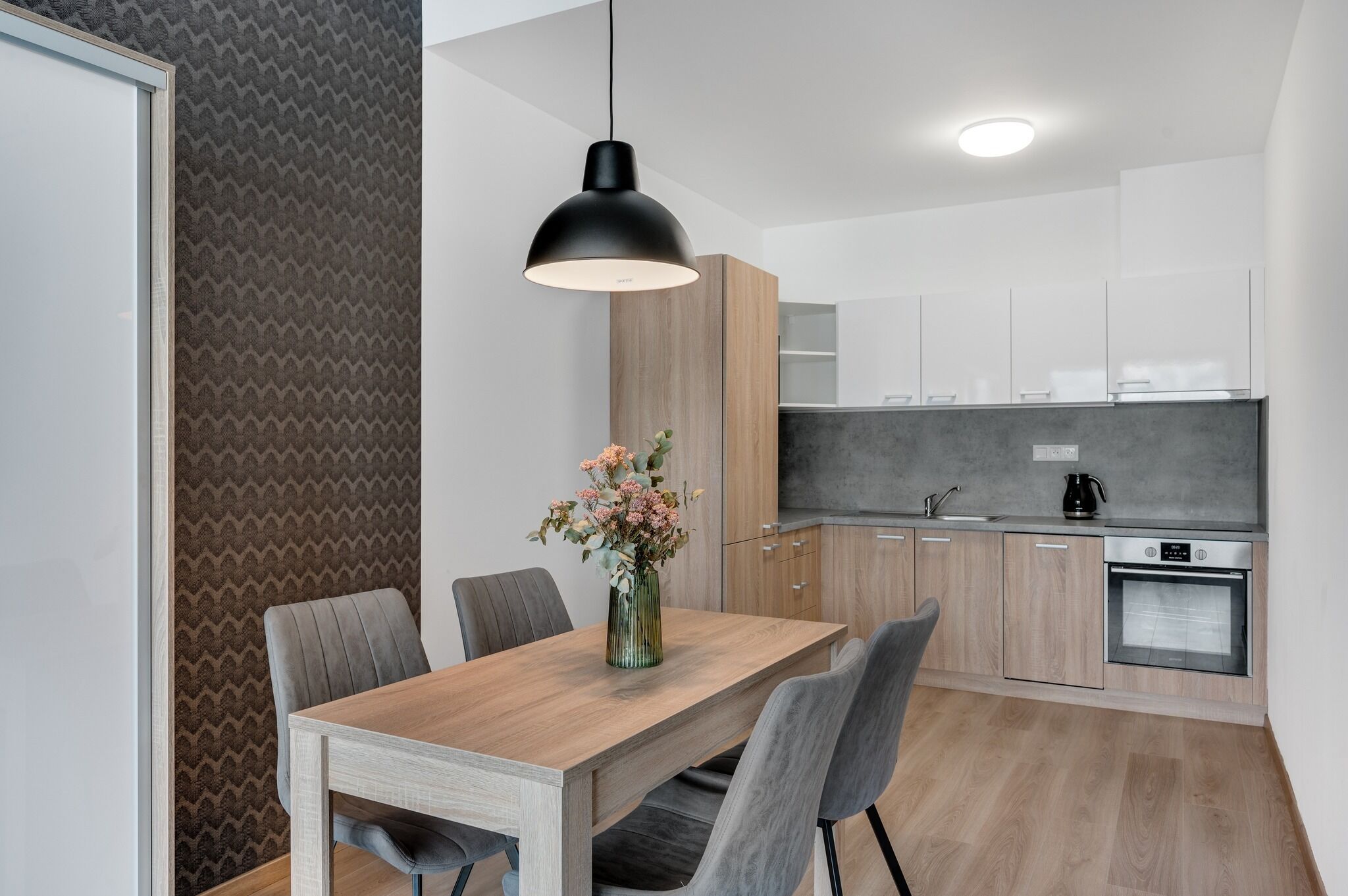 A modern kitchen with wooden cabinets, a built-in oven, and a pendant light above the dining table.