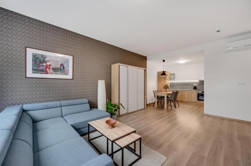 Una sala moderna con un sofá modular, un comedor con mesa y sillas, y una cocina al fondo.