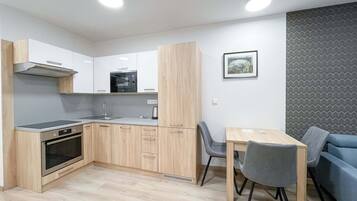 A modern kitchen with wooden cabinets, a built-in oven, and a microwave. There is a dining area with a table and chairs.