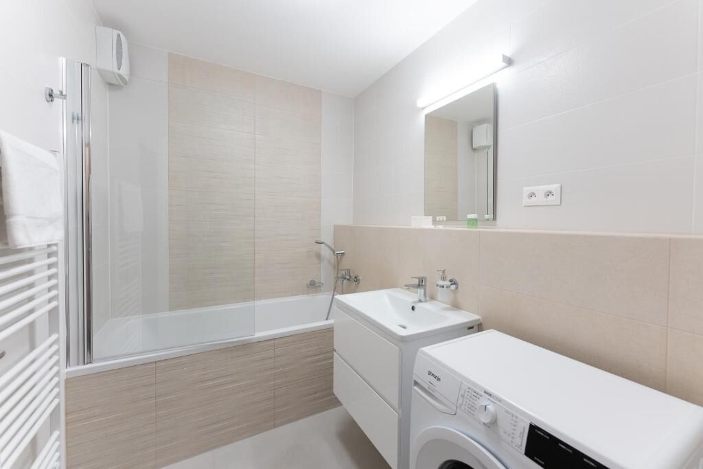 Un baño moderno con cabina de ducha de vidrio, lavamanos blanco y lavadora empotrada.